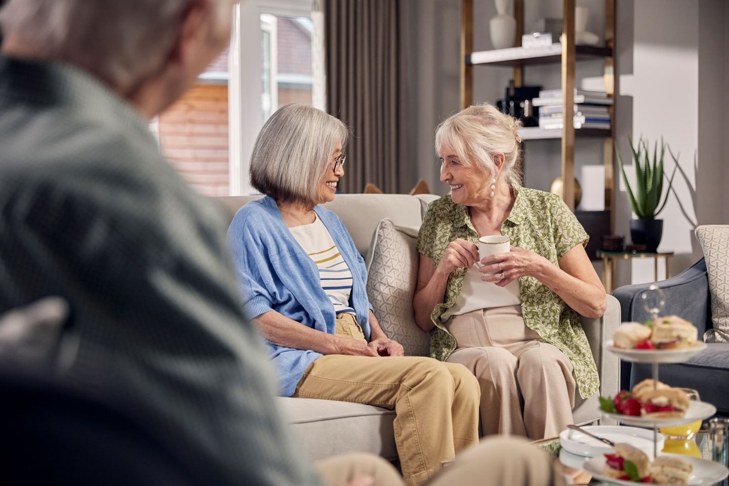 Two older women seating on a sofa and drinking tea