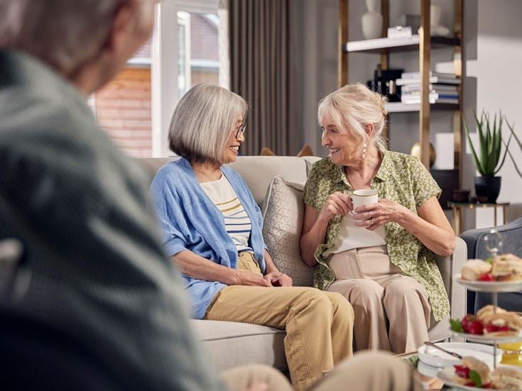 Two older women seating on a sofa and drinking tea