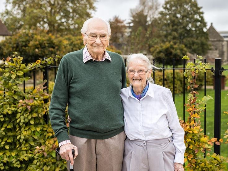 an older couple standing in front of a garden of flowers