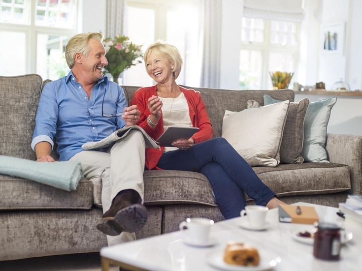 A retired couple sitting on a couch and discussing the cost of a retirement home.