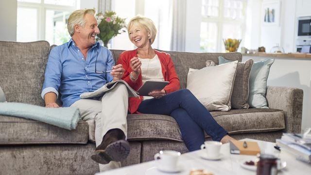 A retired couple sitting on a couch and discussing the cost of a retirement home.