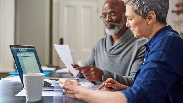 A senior man and woman managing finances with calculator and laptop focusing on pensioners and tax responsibilities