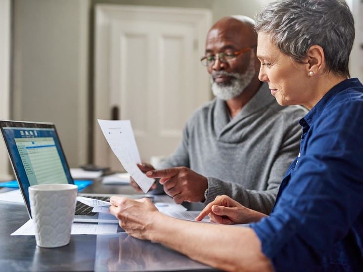 A senior man and woman managing finances with calculator and laptop focusing on pensioners and tax responsibilities