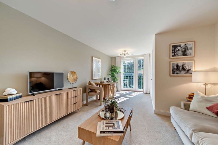 A living room in a McCarthy & Stone retirement property, with a couch, coffee table, and balcony.