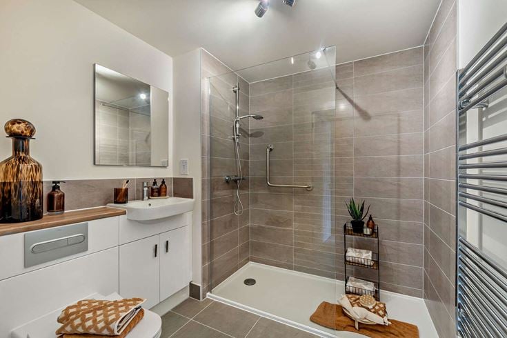 The interior of a bathroom in a McCarthy & Stone retirement home, with a shower, sink, radiator and cabinets.