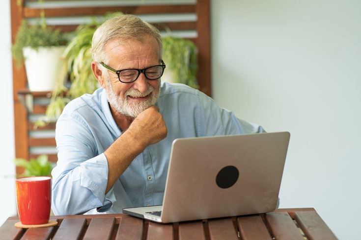 A senior man working on a laptop with a cup of coffee.
