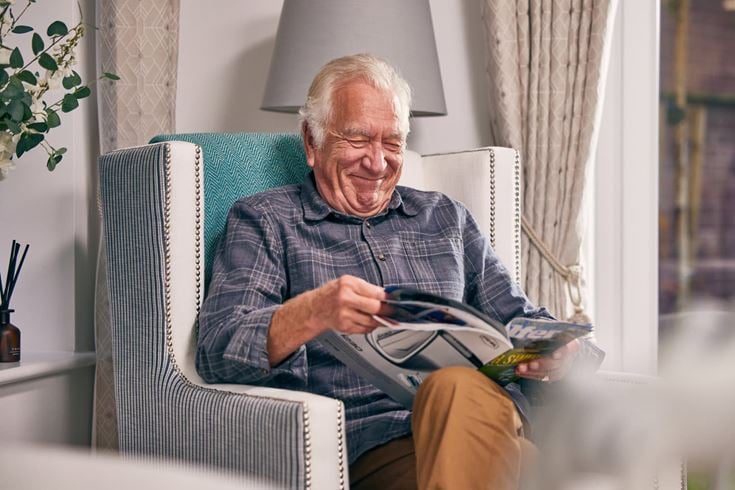An elderly man sitting in a chair reading in a McCarthy & Stone retirement home