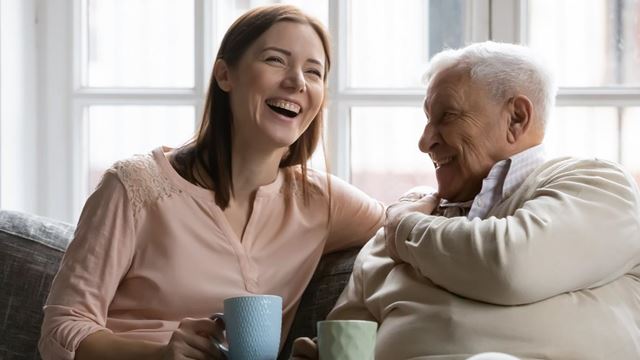 Family members of two generations grown daughter and mature father having fun enjoy tea talk on cozy couch