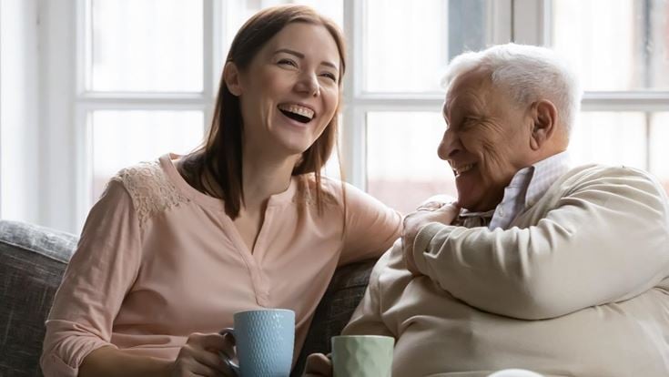 Family members of two generations grown daughter and mature father having fun enjoy tea talk on cozy couch