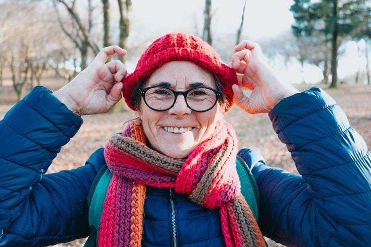 Over 60s retired woman wearing a hat and scarf to keep warm in colder weather.