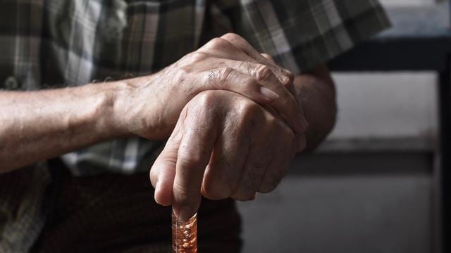 A pair of retiree hands holding a walking stick due to suffering from arthritis.