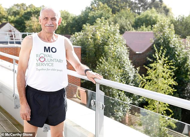 A McCarthy & Stone homeowner and marathon runner poses beside a railing at his retirement home. The retiree wears a white running vest that reads: ‘Together for older people’