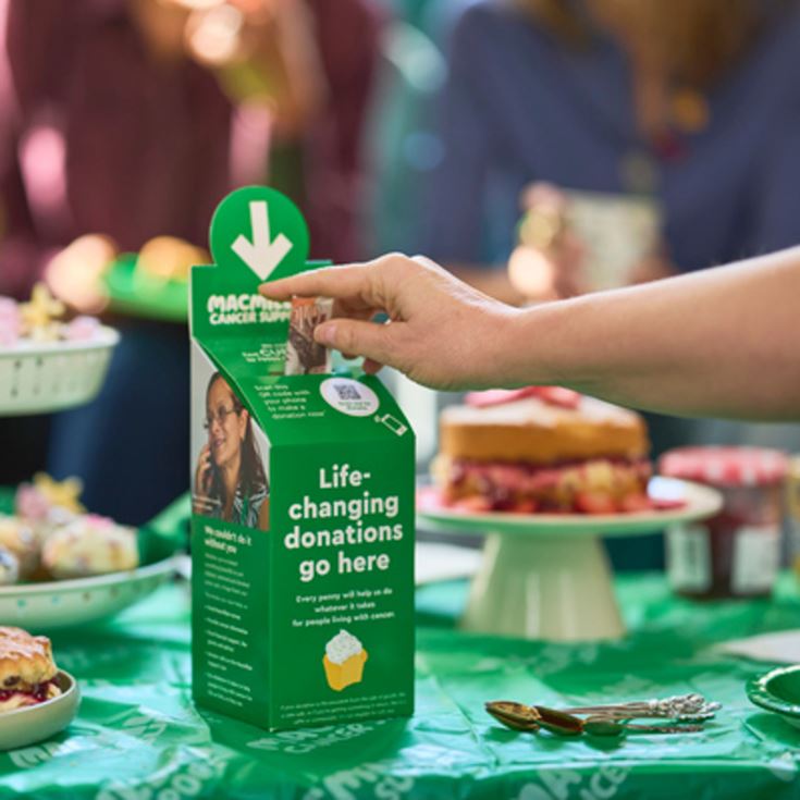 A person putting a £10 note into a donation box at a Macmillan coffee morning held at a retirement home.