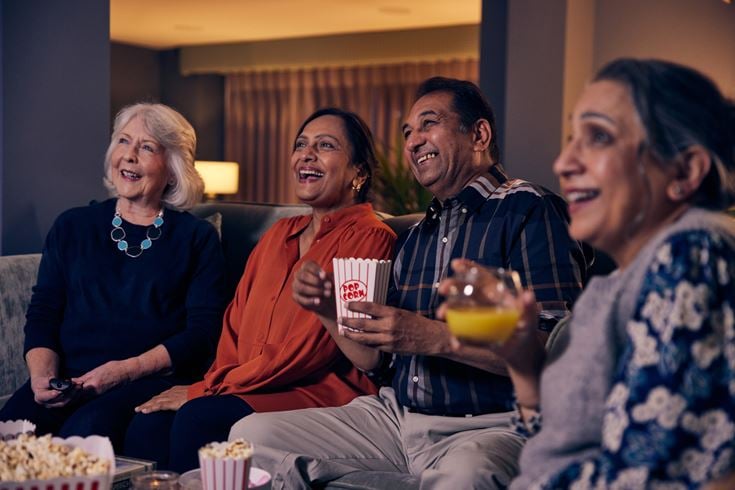 Four retired people enjoy popcorn and drinks while watching a movie.