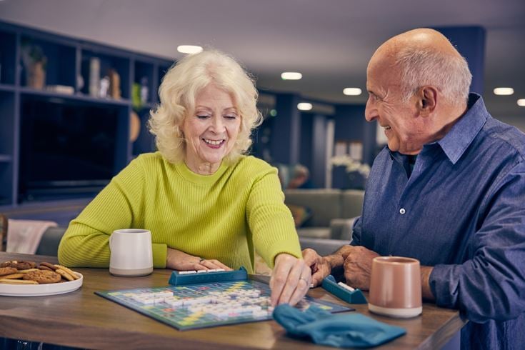 Two retired people play a game of Scrabble with coffee and biscuits.