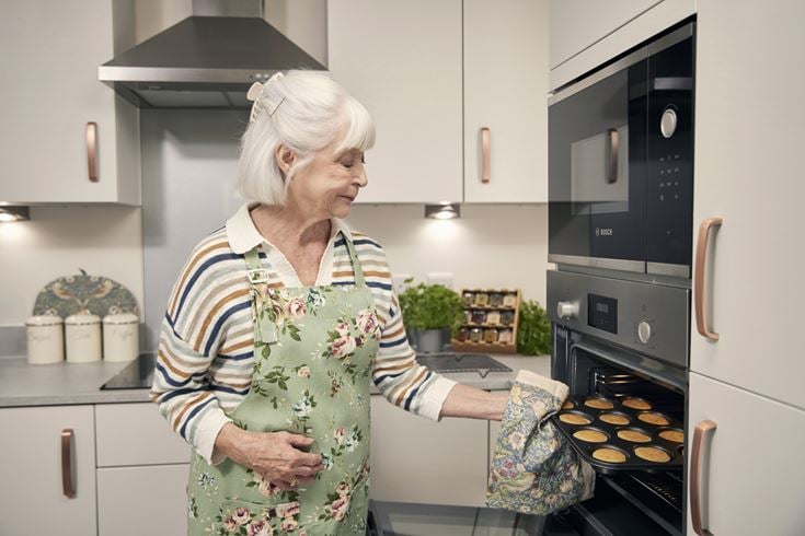 An older lady baking cupcakes in preparation for a bake sale to raise money for charity.