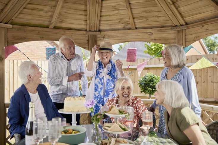 A group of older people laughing and having fun at a summer garden party in a retirement community.