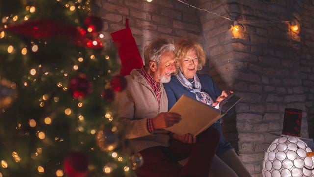 a man and a woman sitting next to a christmas tree looking through photographs