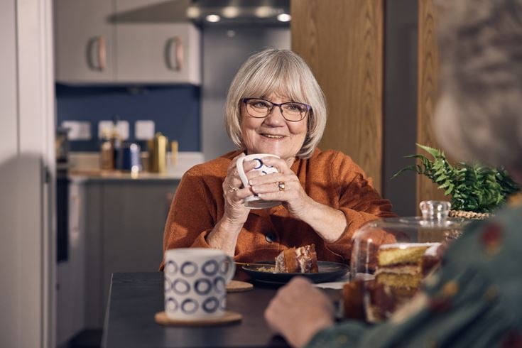 A retired lady catches up with a friend over coffee and a cake.