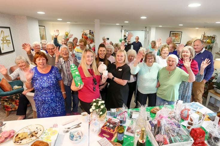 A group of retirees and employees celebrate fundraising for Macmillan Cancer Support with coffee, cake, and raffle prizes.
