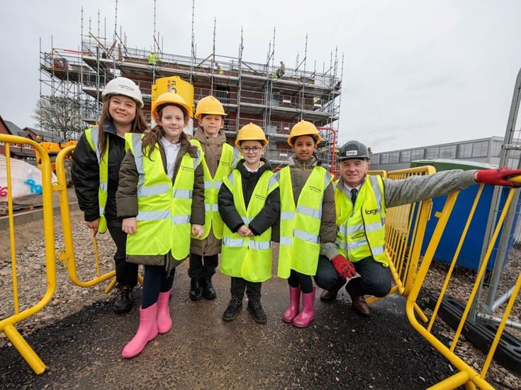 a group of people wearing safety vests and standing next to a yellow machine