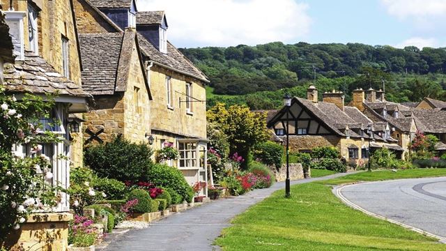 a row of houses with trees in the background with Cotswolds in the background