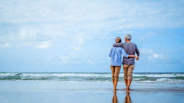 A retired couple walking on the beach.