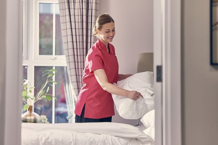 A lady making a bed in a retirement living plus apartment. 