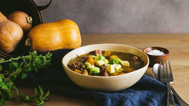 a bowl of soup next to a couple of pumpkins