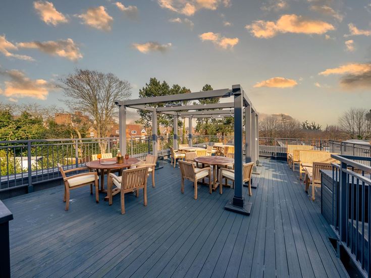 a deck with tables and chairs on it with trees and a sunset in the background