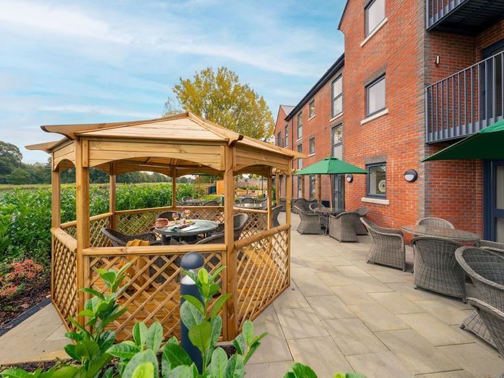 a patio with a table and chairs and a building with a body of water in the background