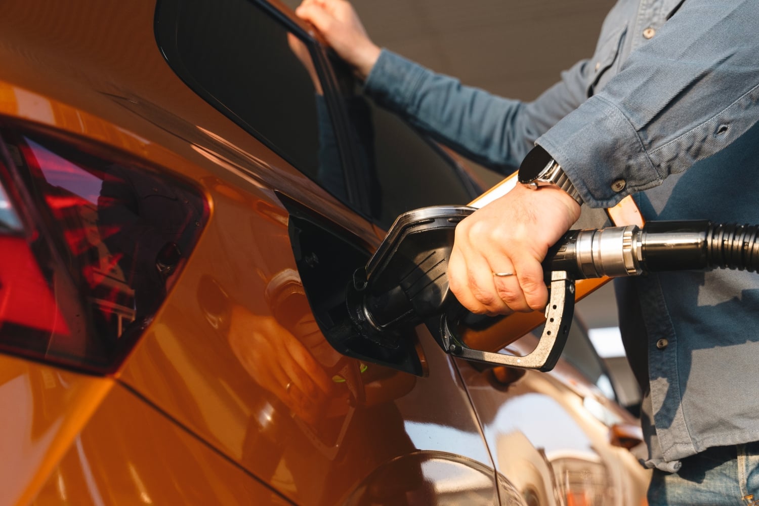 Close-up of a man filling up an orange car at a petrol station.