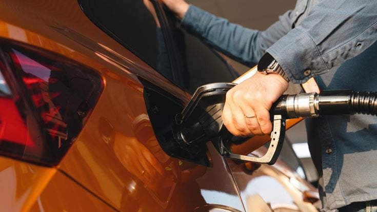 Close-up of a man filling up an orange car at a petrol station.