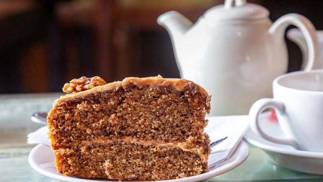 A walnut cake on a plate with a teapot and cup next to it.