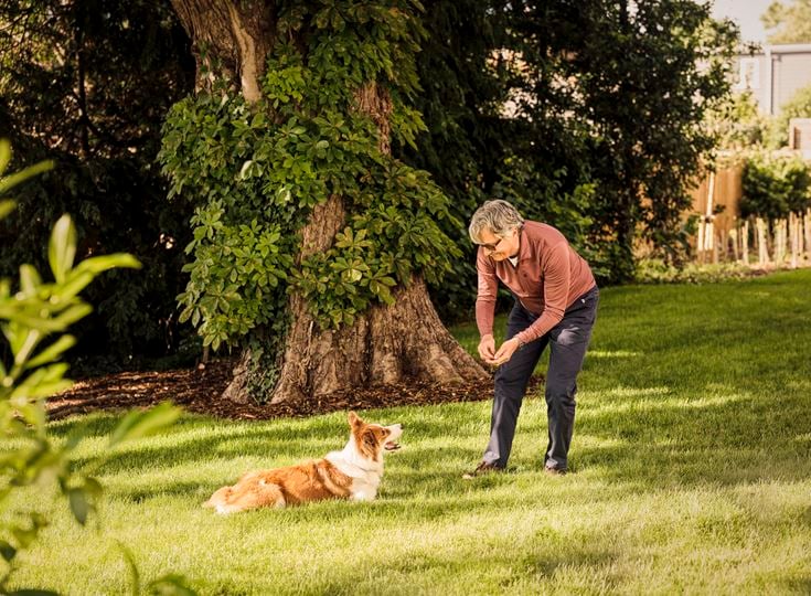 An older man plays with his dog in a field near his retirement property.