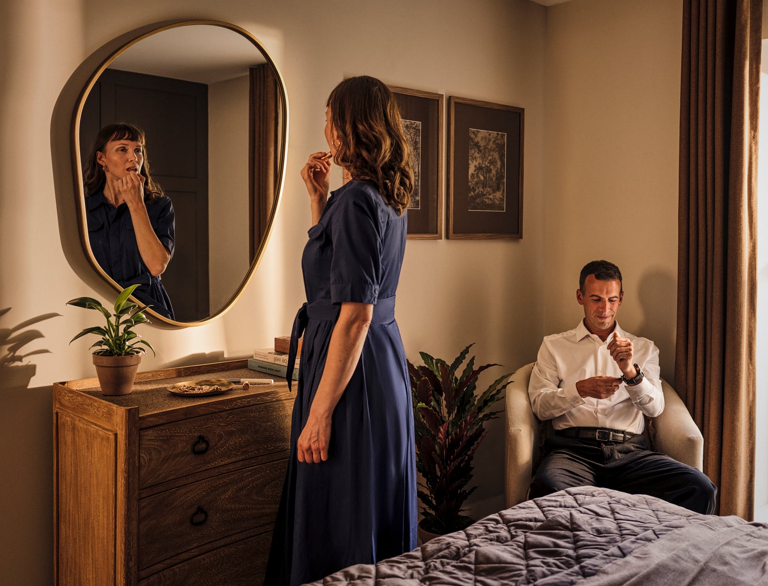 a woman standing in front of a mirror and a man sitting on a bed