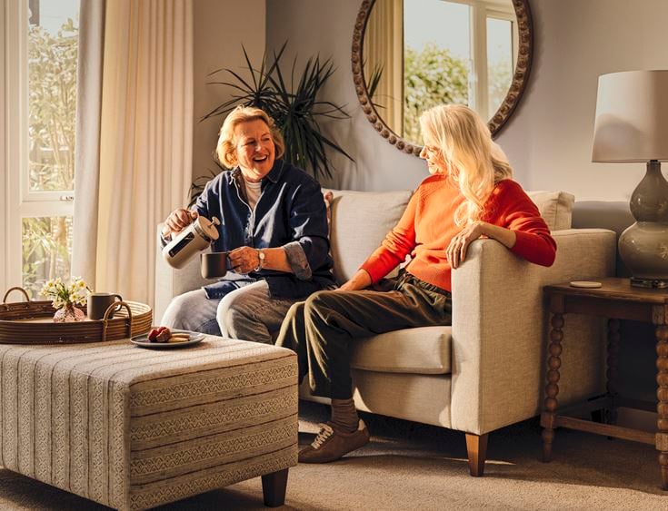 Two retired ladies enjoy coffee in a retirement apartment.