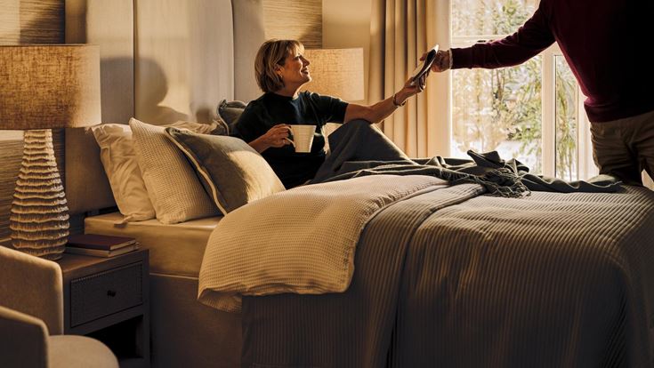 a man and a woman in a room with a bed and a lamp