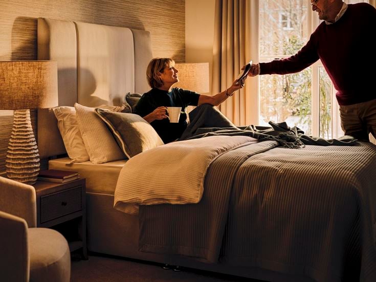 a man and a woman in a room with a bed and a lamp