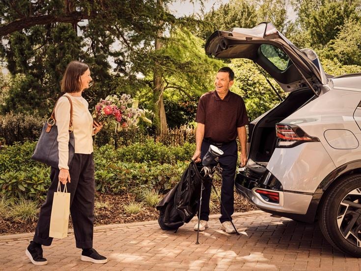 a man and woman standing next to a car with a bag
