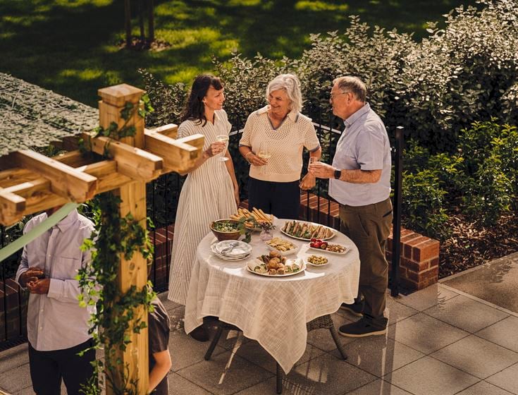 An alderly couple with their adult daughter enjoying food in a McCarthy & Stone garden.