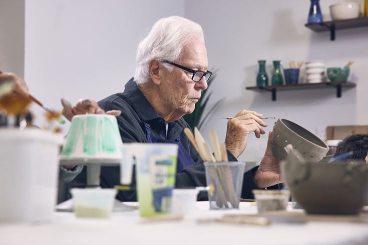 An older man paints homemade pottery.