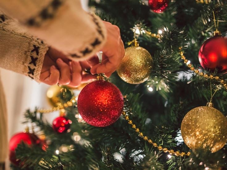 A person hanging a red bauble on a Christmas tree