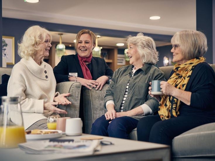 Three retired ladies and a McCarthy & Stone retirement development manager chatting and laughing during a coffee morning.