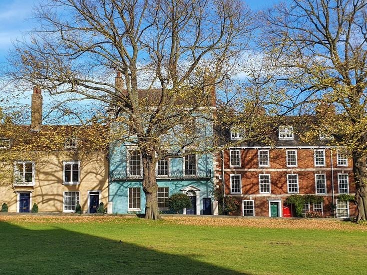 A row of historic buildings in Lincoln along a tree lined street, next to a green field.