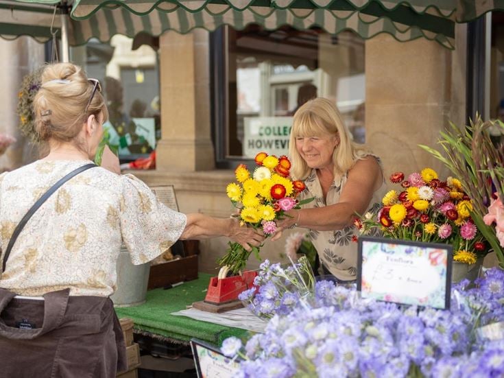 A florist hands a bouquet of flowers to a customer at a market in Stamford, Lincolnshire.