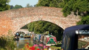 Colourful flowers in front of a canal lined with boats near a bridge.