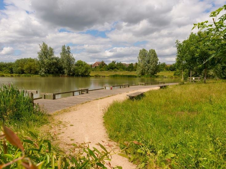 Public seating set among trees and grass overlooking the water in Cambourne.
