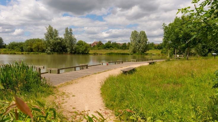 Public seating set among trees and grass overlooking the water in Cambourne.