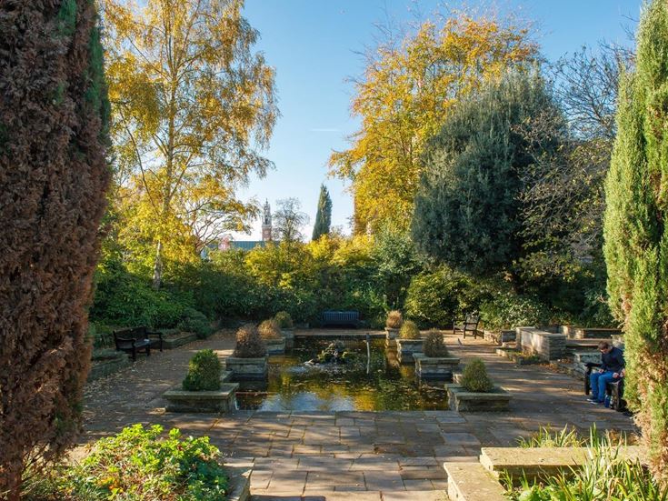 A person sitting on a bench next to the ornamental pond at Castle Park.